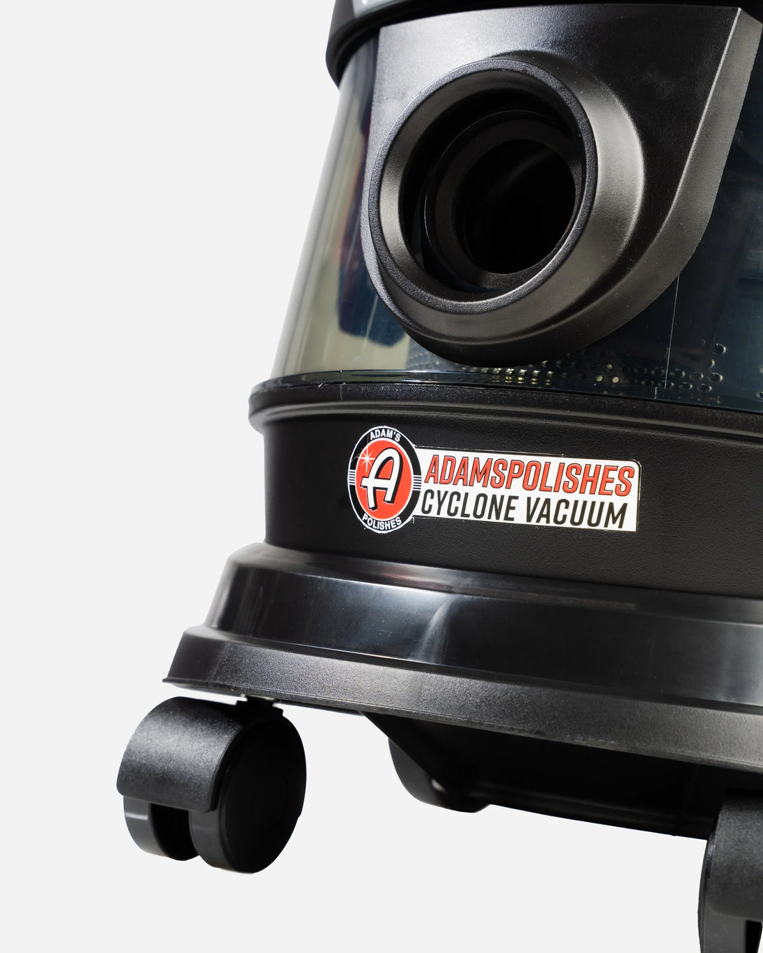 Close-up of a black and dark gray Adamspolishes Cyclone Vacuum cleaner showing the transparent dust container, circular intake opening, and the brand sticker on the front.