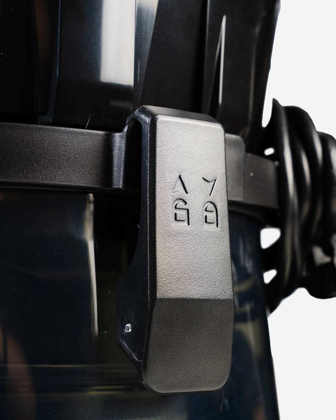 Close-up of a black plastic buckle or latch mechanism with embossed symbols, attached to a dark strap on a light gray background.