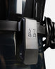 Close-up of a black plastic buckle or latch mechanism with embossed symbols, attached to a dark strap on a light gray background.