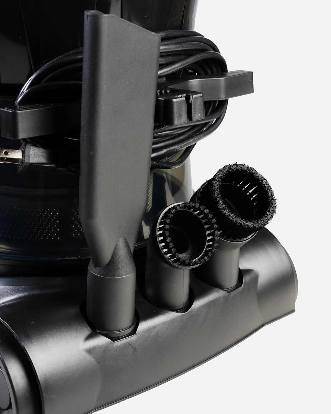 Close-up of a black cordless vacuum cleaner showing its attachments, including a crevice nozzle, a brush head, and a flexible brush attachment, with the power cord coiled behind it.