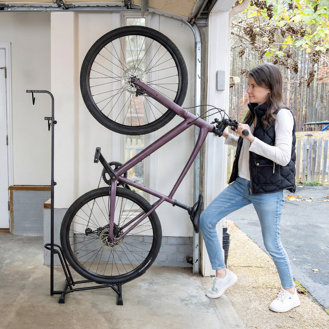 Woman lifting a bicycle with a stand outside a garage