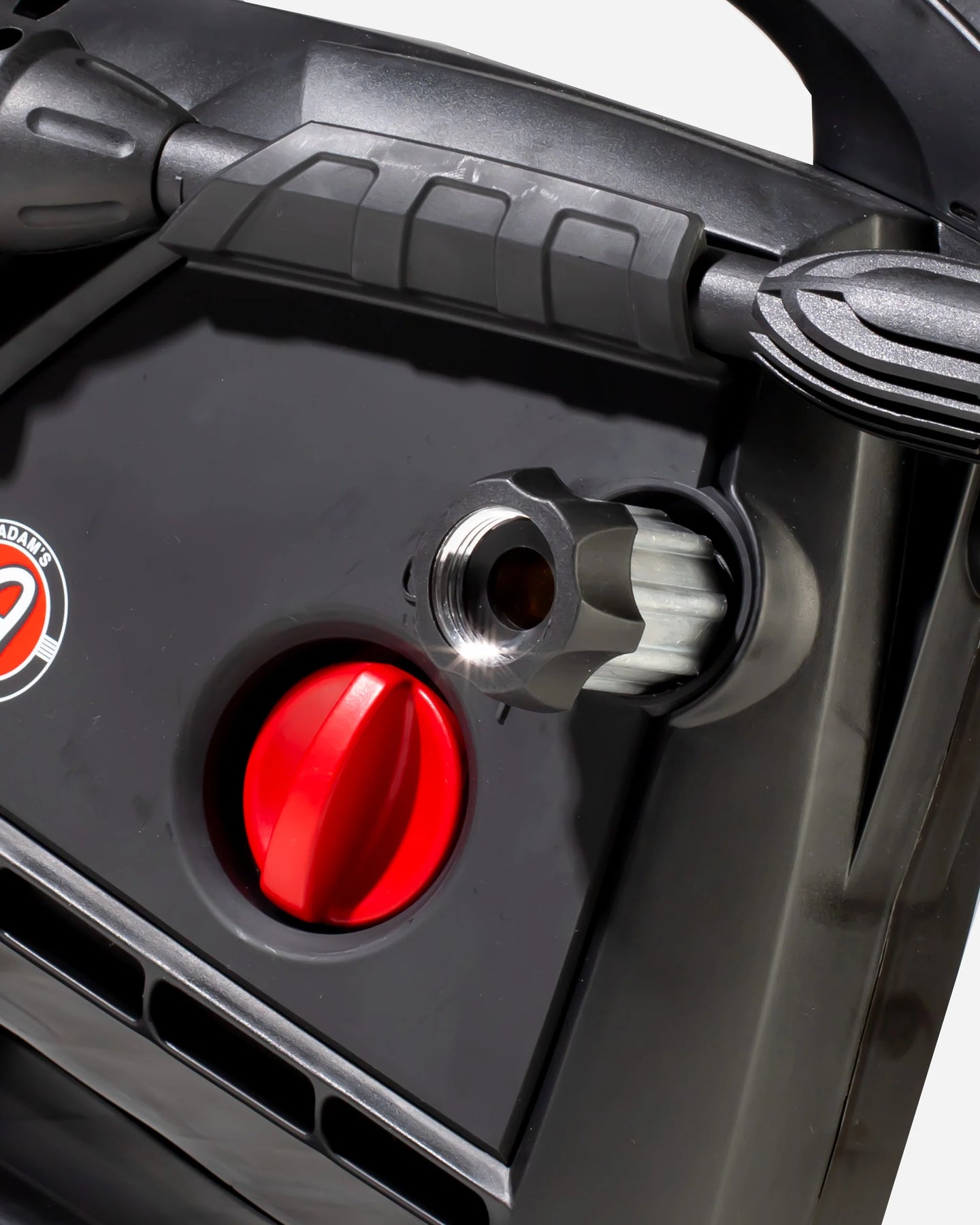 Close-up of a black power washer or pressure washer body with a red dial, a metal port fitting, and part of a black handle against a light gray background.